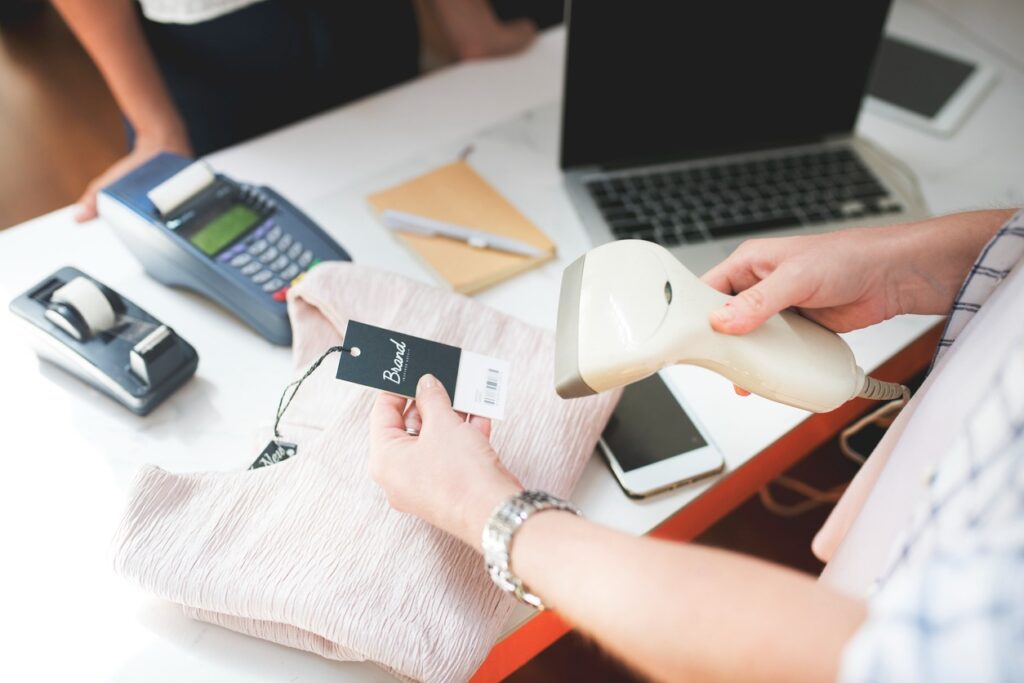 Pessoa usando um scanner para ler o código de barras em uma etiqueta em uma mesa de trabalho com laptop e máquina de cartão de crédito