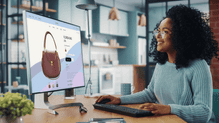 Mulher trabalhando em um escritório moderno, em frente a um monitor com design de marca e cartão, usando computador e avaliando uma apresentação visual.
